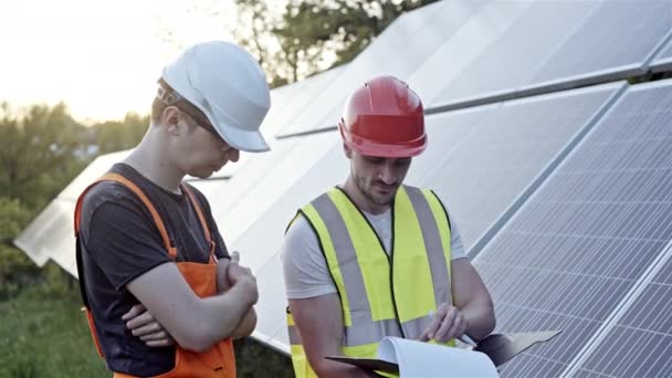 Men in uniform and helmets standing reading papers near solar panels outdoors - Felvétel, videó