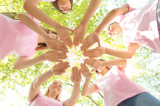Beautiful women of different ages with pink ribbons putting hands together outdoors. Breast cancer concept - Photo, Image