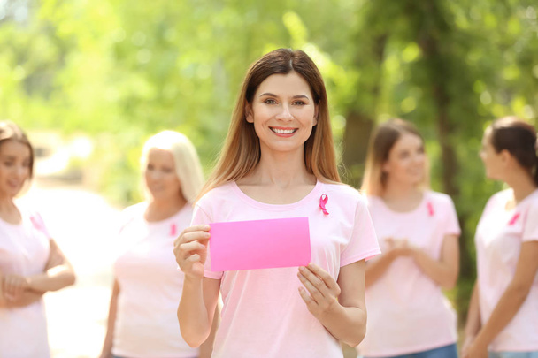Красивая женщина с розовой лентой держит открытку на открытом воздухе. Концепция рака молочной железы
 - Фото, изображение