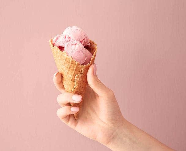 Mujer sosteniendo cono de gofre con delicioso helado de fresa sobre fondo de color
 - Foto, Imagen