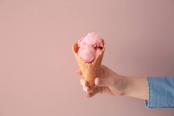 Mujer sosteniendo cono de gofre con delicioso helado de fresa sobre fondo de color
 - Foto, imagen