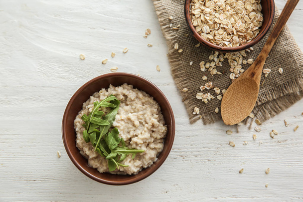 Bowl with tasty oatmeal and arugula on wooden table - Фото, изображение