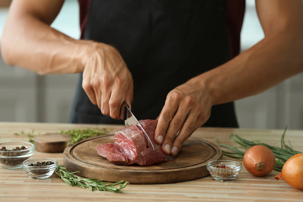 Homme coupant de la viande crue à bord dans la cuisine
 - Photo, image