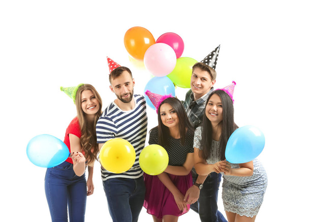 Young people in birthday party caps with balloons on white background - Photo, Image