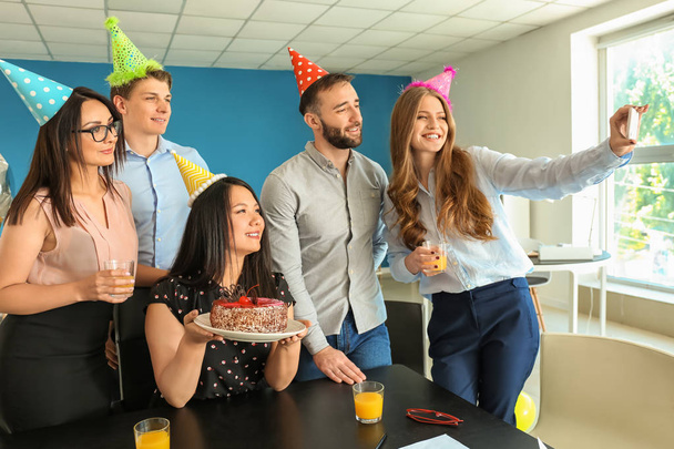 Mujer joven tomando selfie con sus colegas en la fiesta de cumpleaños en la oficina
 - Foto, Imagen