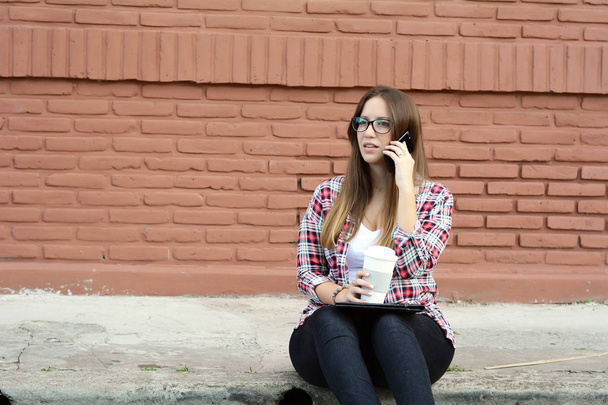 Beautiful woman drinking paper cup of coffee and using a her phone on street. Take away concept - Foto, Imagen