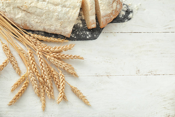 Wheat spikelets with fresh bread on wooden table - Fotoğraf, Görsel