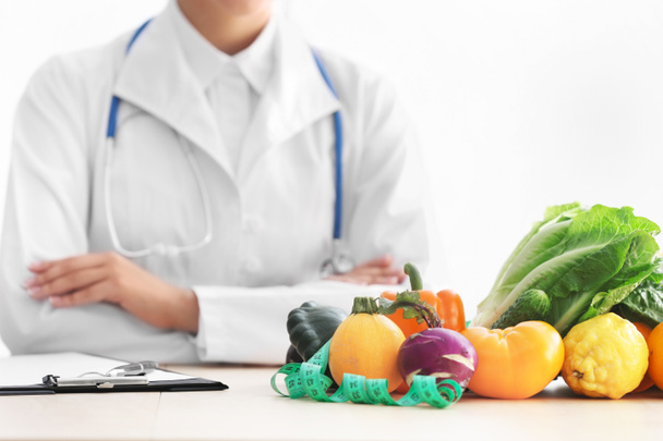 Ernährungsberaterin sitzt am Tisch mit Klemmbrett und gesunden Produkten auf weißem Hintergrund - Foto, Bild