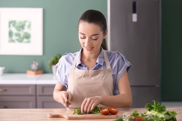 Young woman cutting parsley for salad in kitchen - Foto, imagen