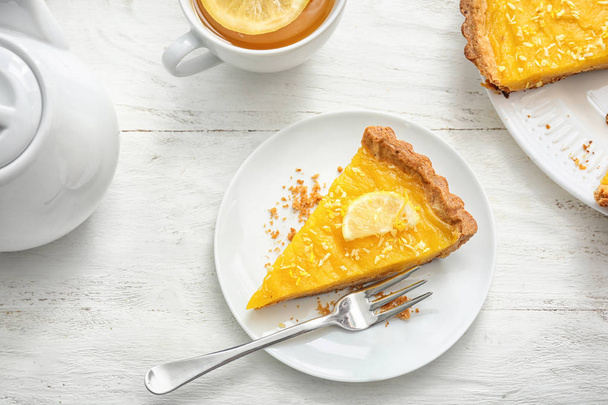 Assiette avec morceau de tarte au citron savoureuse et tasse de thé sur table en bois blanc
 - Photo, image
