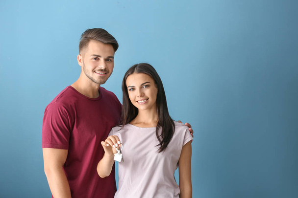 junges glückliches Paar mit Schlüssel ihres neuen Hauses auf farbigem Hintergrund - Foto, Bild