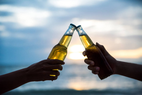Měkké zaostření dva muži řinčení lahví piva dohromady během západu slunce. přátelství den koncept. - Fotografie, Obrázek
