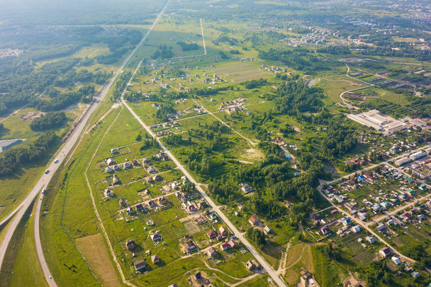 Blick von oben auf ein großes Dorf mit kleinen Häusern, einem grünen Wald und einem großen Feld an einem warmen, sonnigen Sommertag. Hubschrauber-Drohne abgeschossen. - Foto, Bild