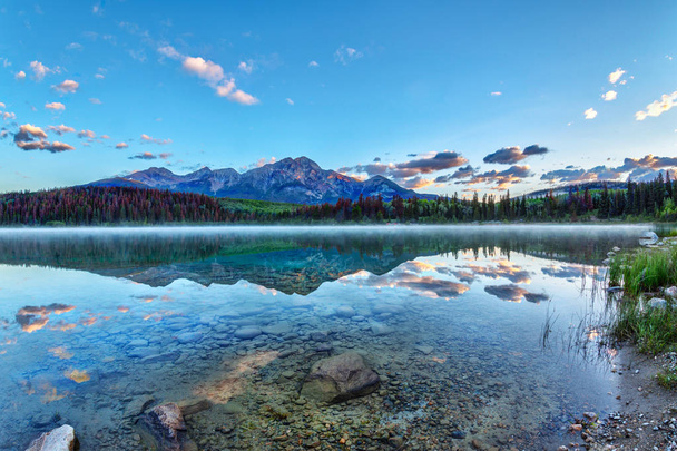 Sunrise over Patricia Lake in Jasper National Park with Pyramid Mountain in the background and misty fog on the water's surface. Calm waters create serene reflections. - Фото, изображение