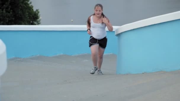 Young fat girl running down stairs, shedding weight, listening to music in headphones concept of healthy lifestyle super slow motion - Πλάνα, βίντεο