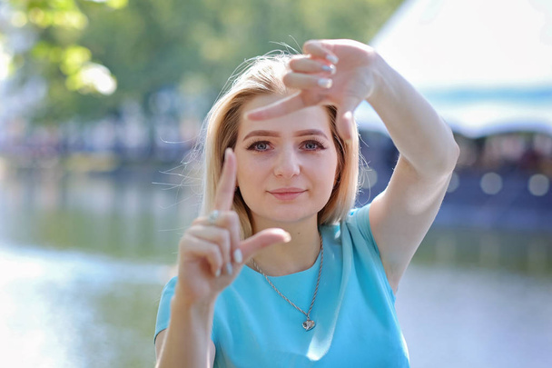 Portrait of beautiful young woman with blond hair and long eyelashes, making photo gesture. Summer outdoors - Photo, Image
