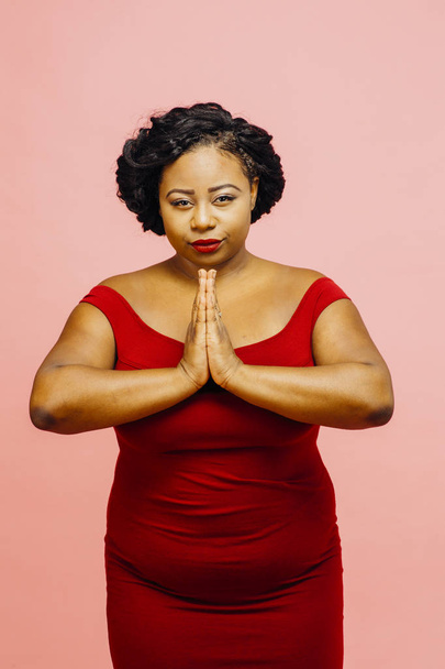 Inner peace/ Young woman in red looking at camera and hands together, isolated on pink background - Foto, afbeelding