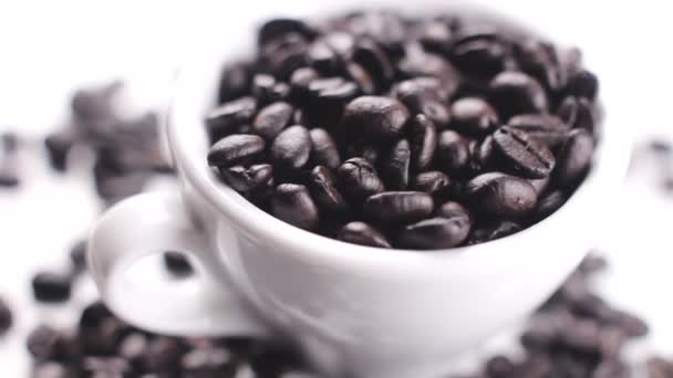 Black coffee beans in white cup rotating on white surface. Close up. - Felvétel, videó