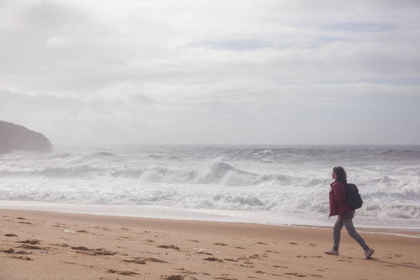 Girl traveler walks along the Atlantic coast with waves in cloudy winter weather - Foto, imagen