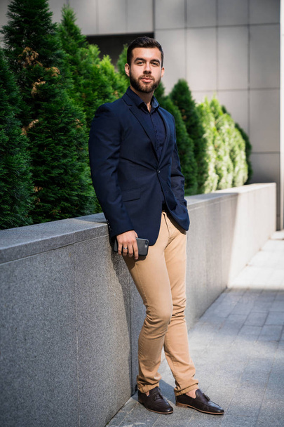 Впевнений молодий бізнесмен в синьому костюмі, використовуючи стоячи в місті. Бізнесмен має гальма і дивиться на камеру за межами офісу
. - Фото, зображення