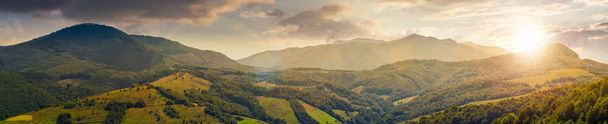 Panorama des wunderschönen Bergrückens bei Sonnenuntergang im Abendlicht. perfekte Landschaft. ländlichen Feld auf den nächsten bewaldeten Hügeln. mächtiger Borzhava-Kamm in der Ferne - Foto, Bild