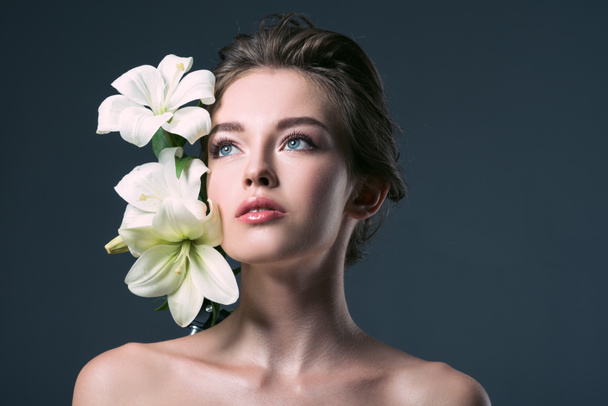 close-up portrait of beautiful young woman with white lilies looking away isolated on grey - Фото, изображение
