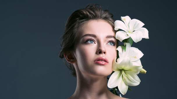 close-up portrait of attractive young woman with white lilies looking away isolated on grey - Foto, immagini