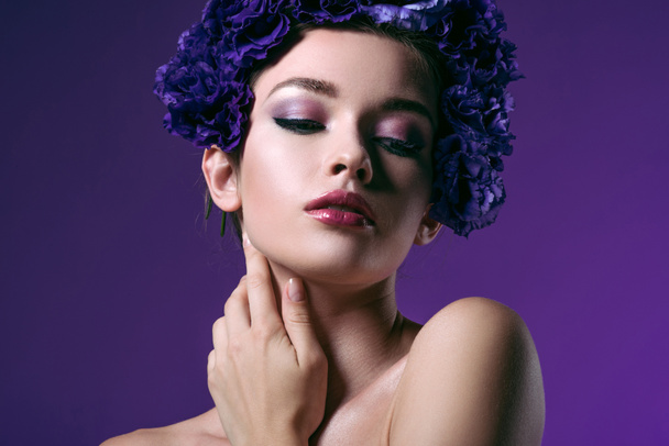close-up portrait of tender young woman with eustoma flowers wreath on head looking at camera isolated on purple - Photo, image