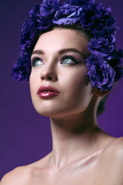close-up portrait of attractive young woman with eustoma flowers wreath on head looking away isolated on purple - Фото, изображение