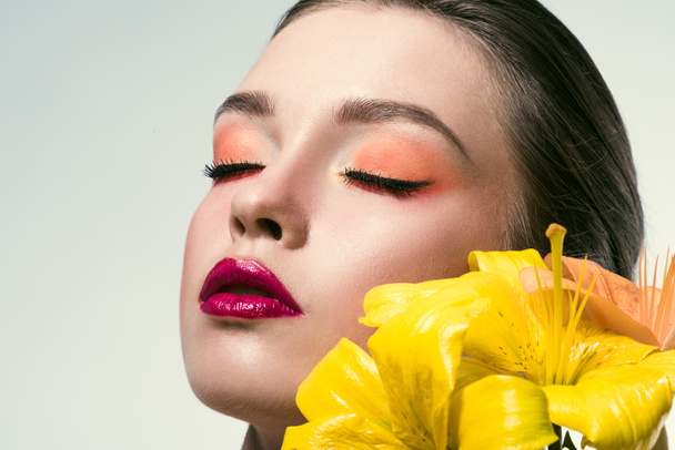 retrato de cerca de la hermosa mujer joven con maquillaje de moda y flores de lilium amarillo aislado en blanco
 - Foto, Imagen