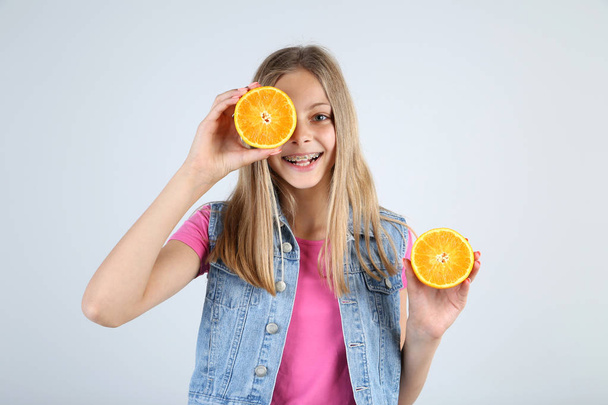 Young smiling girl with orange fruit on grey background - Foto, Imagen
