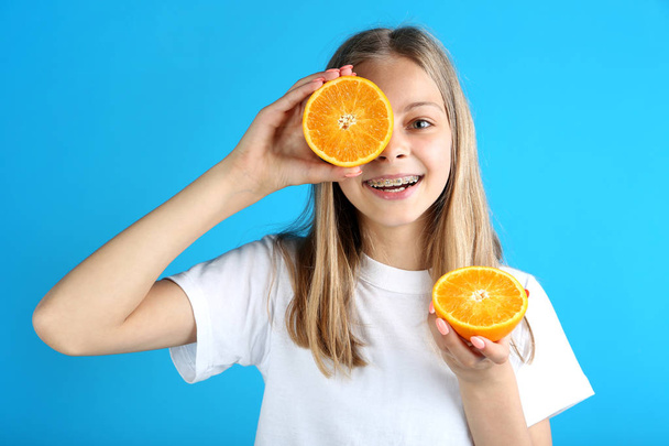 Young smiling girl with orange fruit on blue background - Fotoğraf, Görsel