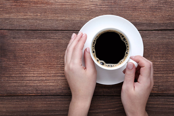 Female hands holding cup of coffee on wooden background - Photo, Image