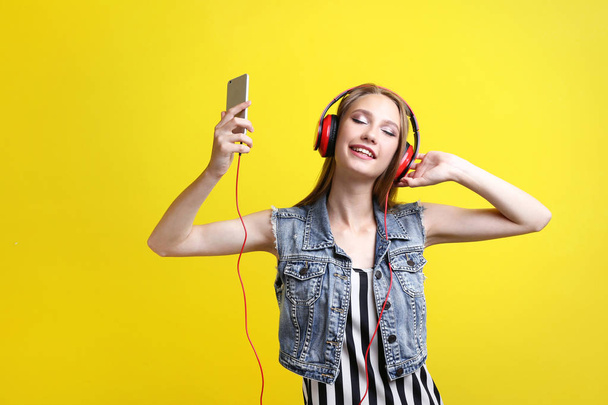 Young woman with headphones and smartphone on yellow background - Fotó, kép