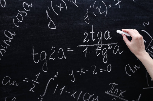 Female hand writing maths formulas on chalkboard - Foto, imagen