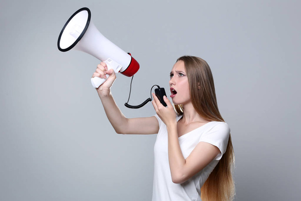 Young woman screaming in megaphone on grey background - Φωτογραφία, εικόνα
