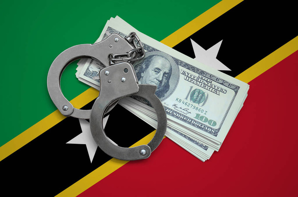 Saint Kitts and Nevis flag  with handcuffs and a bundle of dollars. Currency corruption in the country. Financial crimes. - Photo, Image