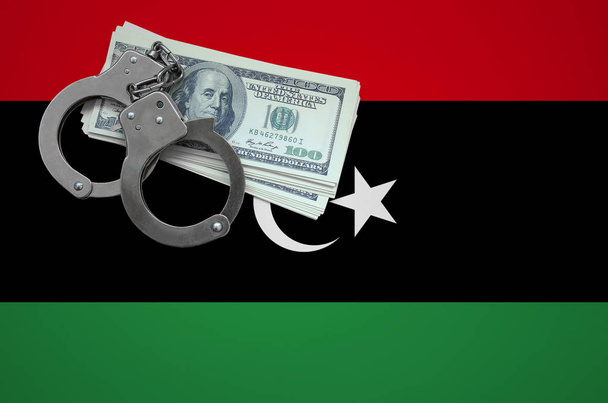 Σημαία της Λιβύης με χειροπέδες και μια δέσμη των δολαρίων. Η έννοια του σπασίματος των εγκλημάτων νόμου και κλέφτες. - Φωτογραφία, εικόνα