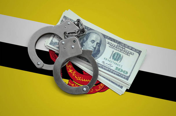 Σημαία του Μπρουνέι Darussalam με χειροπέδες και μια δέσμη των δολαρίων. Νόμισμα της διαφθοράς στη χώρα. Οικονομικά εγκλήματα. - Φωτογραφία, εικόνα