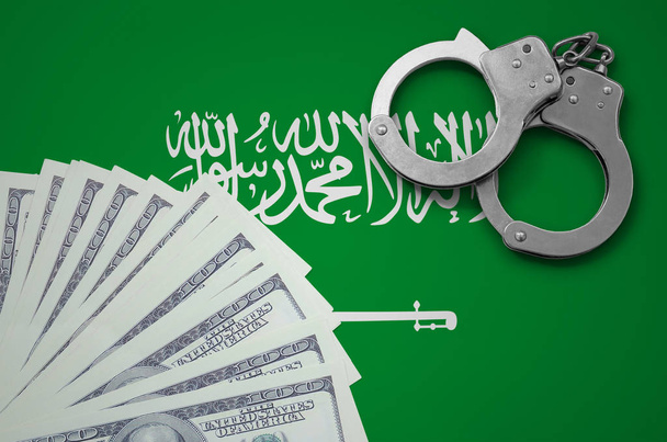 Σημαία της Σαουδικής Αραβίας με χειροπέδες και μια δέσμη των δολαρίων. Η έννοια της παράνομης τραπεζικές εργασίες μας νόμισμα. - Φωτογραφία, εικόνα