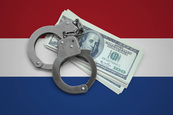 Niederländische Flagge mit Handschellen und einem Bündel Dollars. Währungskorruption im Land. Finanzverbrechen. - Foto, Bild