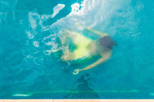 Blick von oben auf einen jungen Mann, der in einem Schwimmbad unter Wasser schwimmt - Foto, Bild