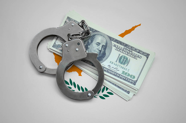 Кипрский флаг с наручниками и пачкой долларов. Коррупция валюты в стране. Финансовые преступления
. - Фото, изображение