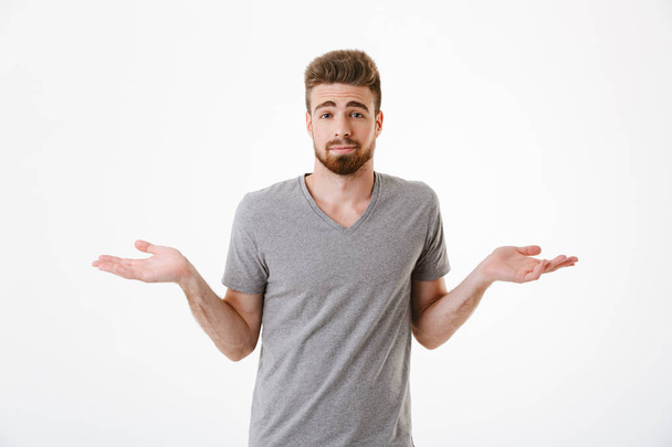 Image of confused young man standing isolated over white wall background looking camera. - 写真・画像