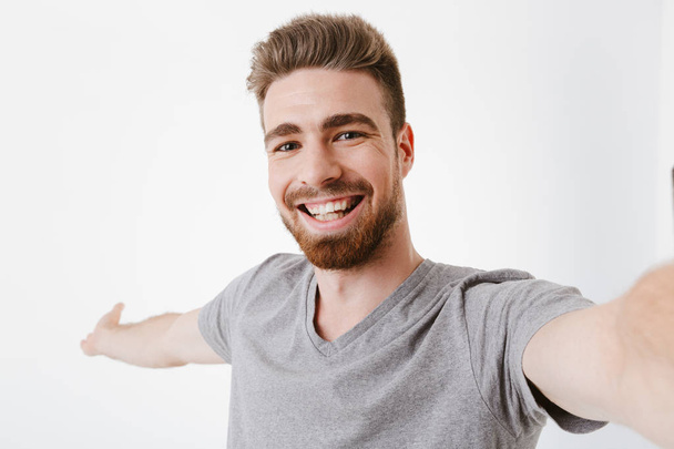 Portrait of a cheerful young bearded man taking a selfie isolated over white background - Foto, imagen