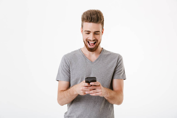 Image of happy handsome young man standing isolated over white wall background using mobile phone. - Φωτογραφία, εικόνα