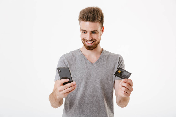 Állandó elszigetelt fehér háttér holding hitelkártyát használ mozgatható telefon mint boldog vidám fiatalember képe. - Fotó, kép