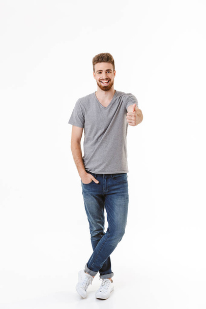 Image of handsome happy young man standing isolated over white wall background looking camera make thumbs up gesture. - Fotó, kép
