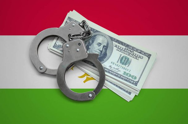 Tadzjikistan vlag met handboeien en een bundel die van dollars. De corruptie van de valuta in het land. Financiële misdrijven. - Foto, afbeelding