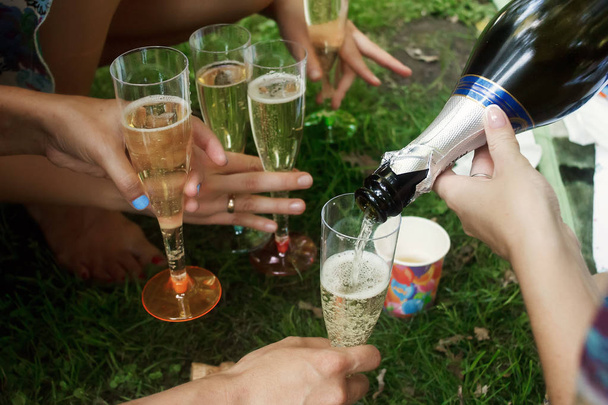 hands of woman holding colorful glasses and pouring champagne at joyful party in summer park, bridal shower or wedding reception - Foto, afbeelding